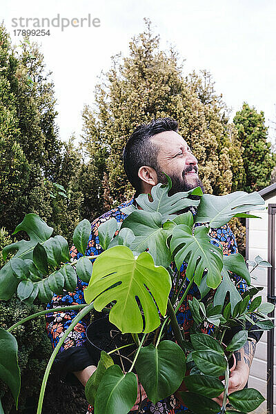 Lächelnder Mann mit Topfpflanzen im Hinterhof