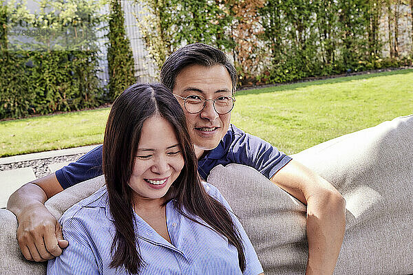 Smiling mature man wearing eyeglasses by woman sitting on sofa