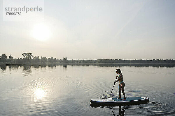 Frau macht Standup-Paddleboarding im See bei Sonnenuntergang