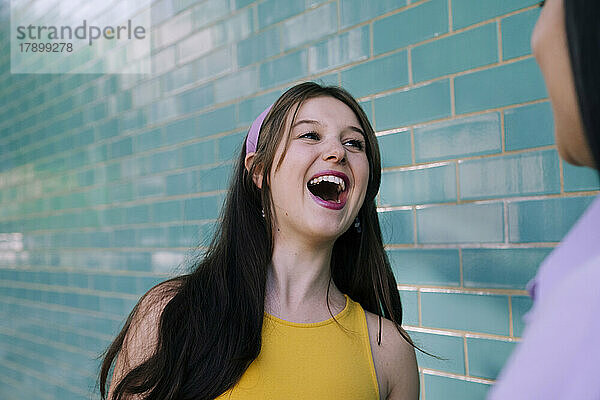 Young woman laughing looking at friend by wall