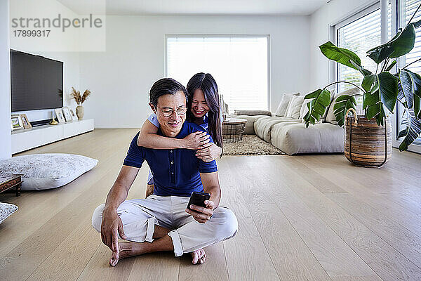 Glückliche Frau mit Arm um Mann und Smartphone auf dem Boden zu Hause