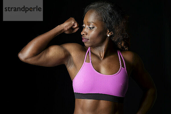 Sportlerin im rosafarbenen Sport-BH lässt Muskeln vor schwarzem Hintergrund spielen