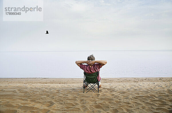 Älterer Mann sitzt auf einem Klappstuhl und entspannt sich am Strand