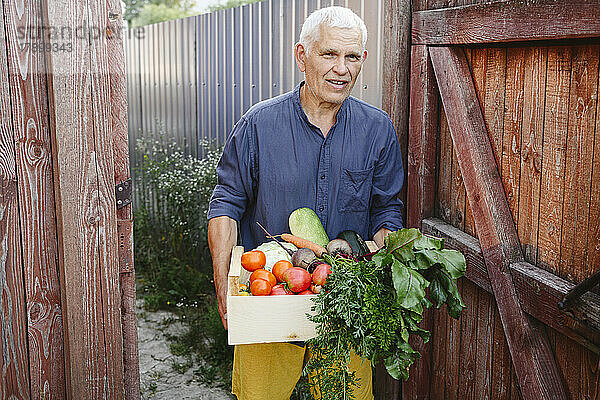 Älterer Mann mit frischem Gemüse in Holzkiste vor der Tür