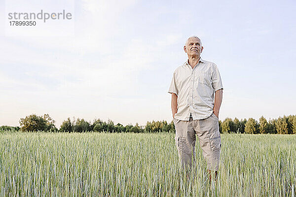 Senior farmer standing with hands in pockets at farm
