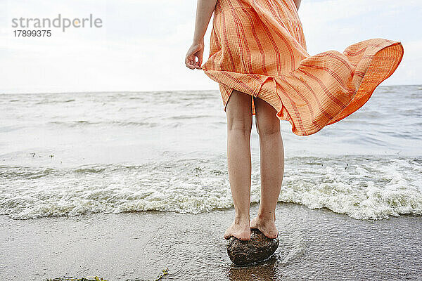 Mädchen steht auf Stein am Meeresufer