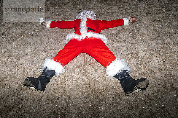 Mann im Weihnachtsmannkostüm liegt im Sand am Strand