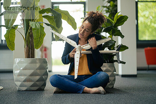 Geschäftsfrau mit geschlossenen Augen hält Windturbinenmodell im Büro