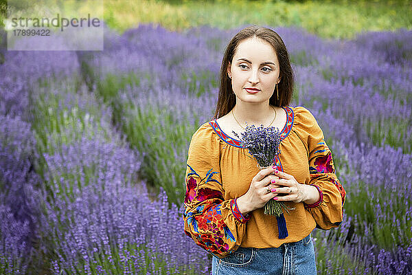 Lächelnde Frau mit einem Strauß Lavendelblüten steht auf dem Feld