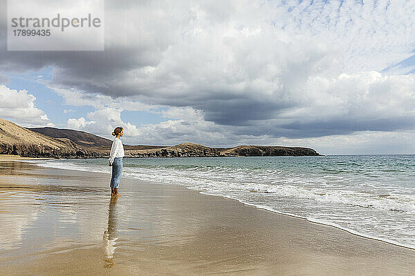 Junge Frau blickt an einem sonnigen Tag auf das Meer