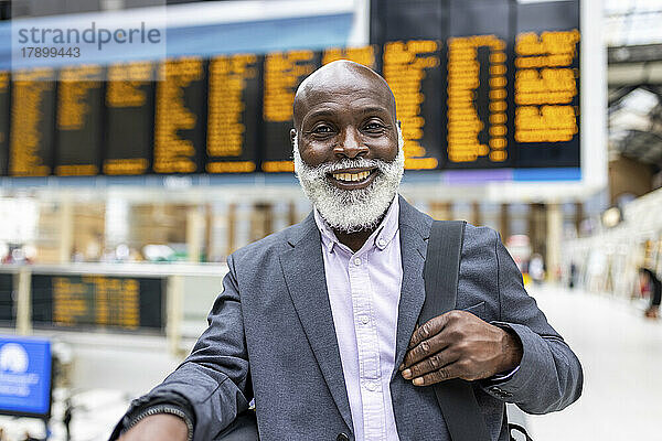 Lächelnder älterer Geschäftsmann mit Laptoptasche am Bahnhof