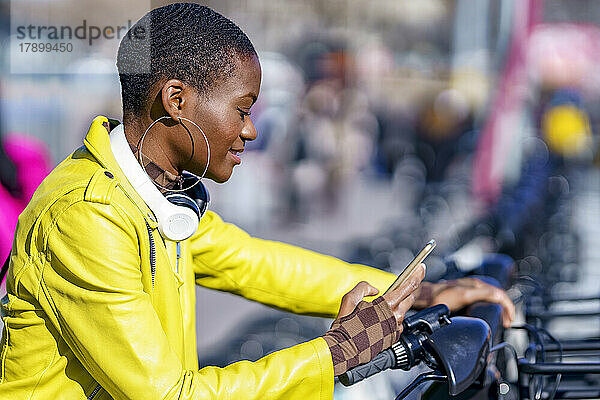 Frau mit Smartphone mietet Fahrrad am Parkplatz