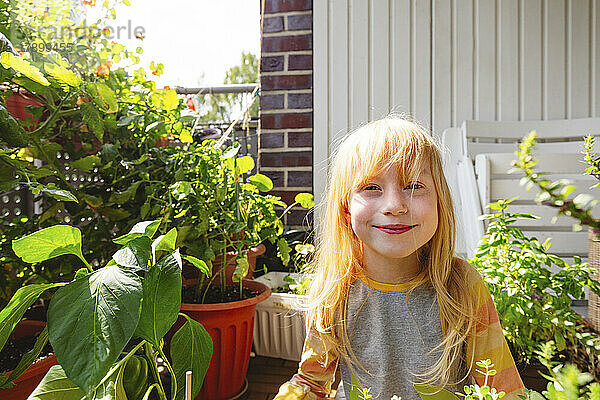 Glückliches Mädchen  das inmitten einer Pflanze auf dem Balkon steht