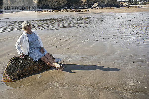 Nachdenkliche Frau sitzt auf einem Felsen am Strand