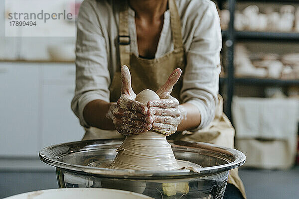 Hände einer Kunsthandwerkerin  die in der Werkstatt Ton auf einer Töpferscheibe formt