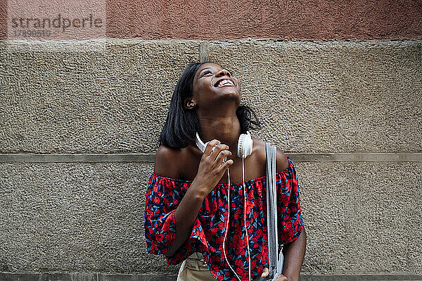 Fröhliche Frau mit Kopfhörern  die vor der Wand nach oben schaut