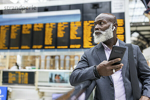 Leitender Geschäftsmann mit Smartphone  der am Bahnhof Musik hört