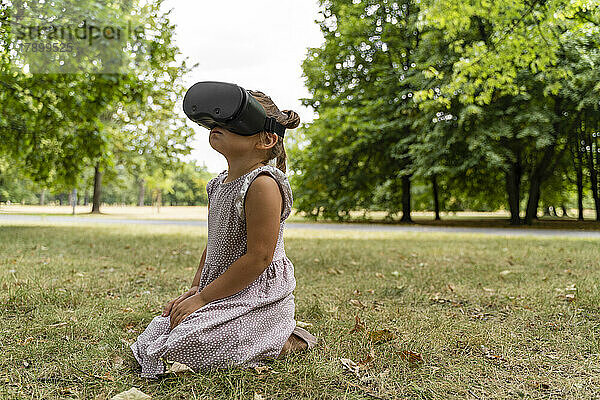 Girl wearing virtual reality simulator kneeling on grass at park
