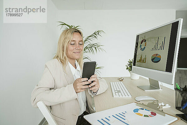 Geschäftsfrau benutzt Mobiltelefon am Schreibtisch im Büro