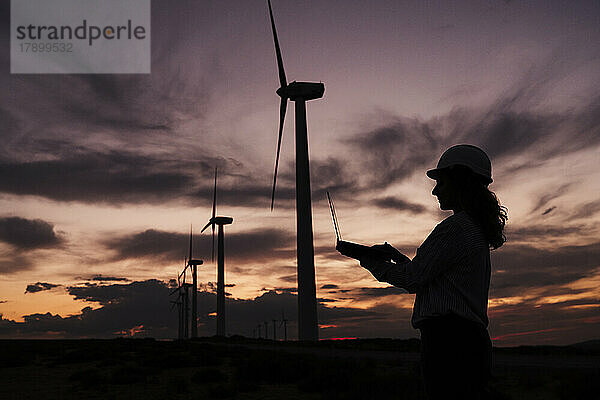 Silhouette eines Ingenieurs  der am Laptop neben Windkraftanlagen im Windpark arbeitet