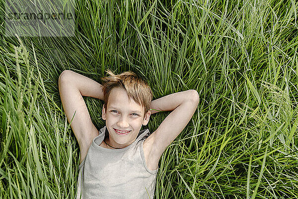 Smiling boy lying down with hands behind head on grass