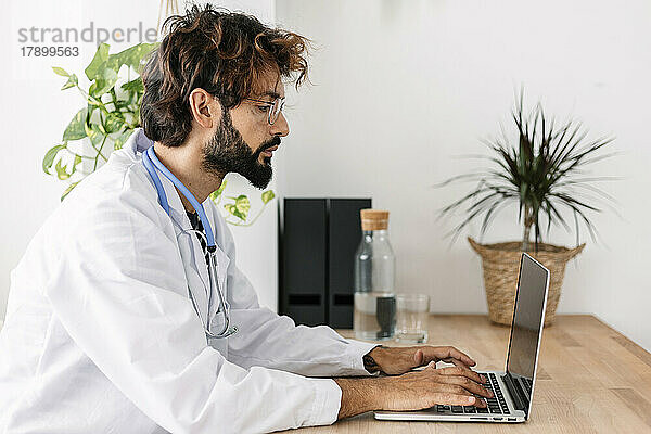 Arzt arbeitet am Laptop und sitzt am Schreibtisch im Heimbüro