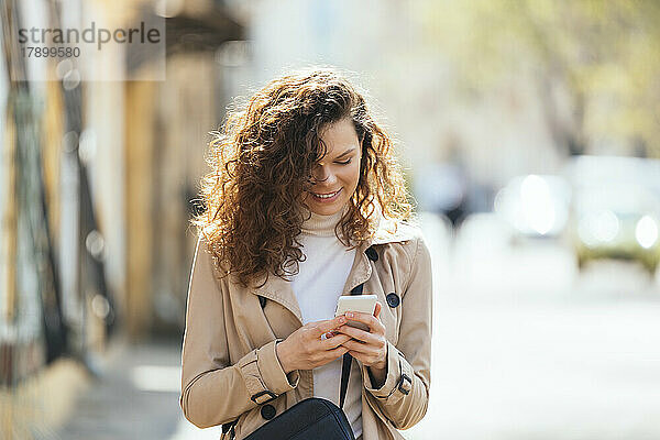 Glückliche Frau  die an einem sonnigen Tag ihr Mobiltelefon benutzt