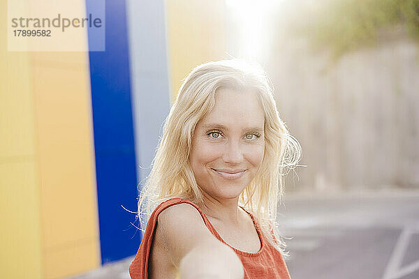 Lächelnde junge Frau mit blonden Haaren an einem sonnigen Tag