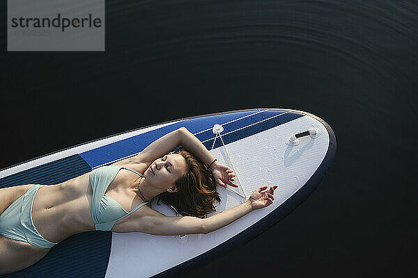 Frau mit geschlossenen Augen liegt auf einem Paddleboard über dem Wasser