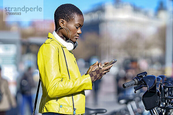 Junge Frau benutzt Smartphone am Fahrradparkplatz