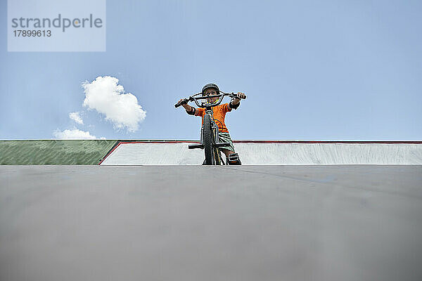 Junge mit BMX-Fahrrad im Skateboardpark vor dem Himmel