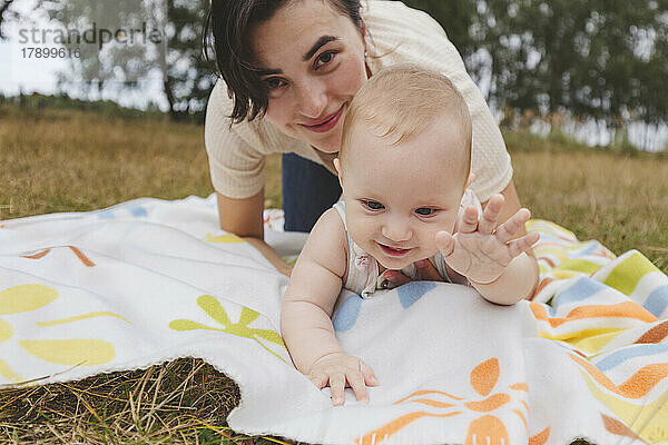 Verspielte Mutter und Tochter haben Spaß beim Sitzen auf der Picknickdecke im Park
