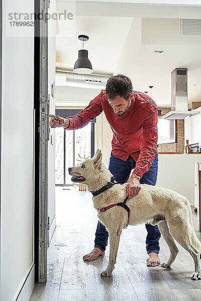 Mann hält Hund an der Leine und öffnet die Tür