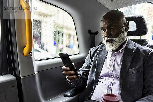 Älterer Passagier benutzt Mobiltelefon auf dem Rücksitz eines Taxis