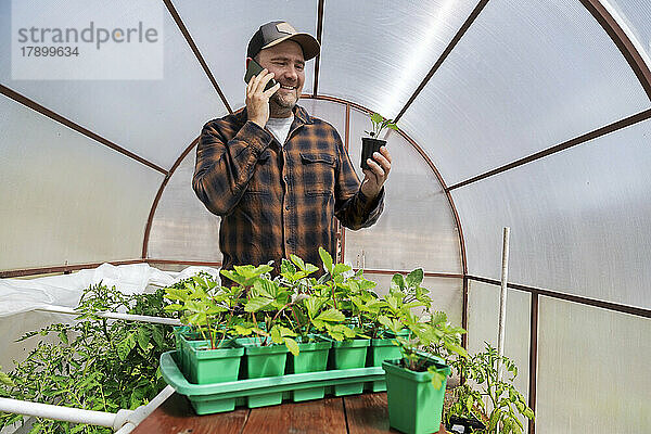 Smiling farmer holding potted plant talking on mobile phone