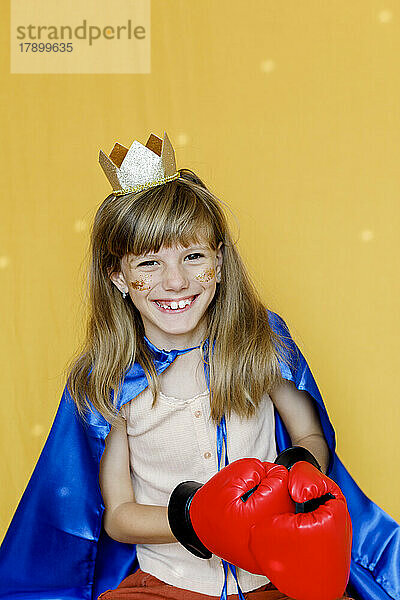 Cute girl wearing crown and boxing gloves against yellow background