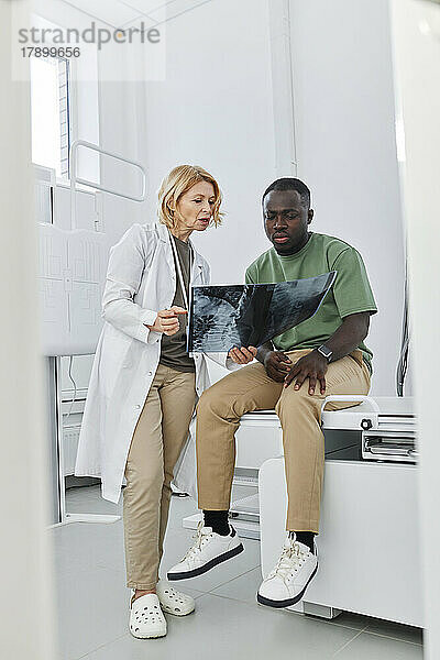Arzt erklärt dem in der Klinik sitzenden Patienten das Röntgenbild
