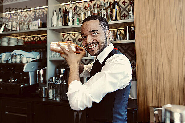 Lächelnder Barkeeper schüttelt Cocktailshaker an der Bar