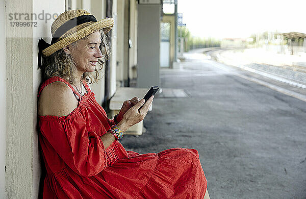 Frau sitzt am Bahnhof und benutzt Smartphone