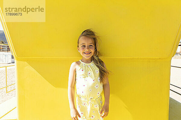 Glückliches Mädchen  das vor der gelben Wand in der Rettungsschwimmerhütte steht
