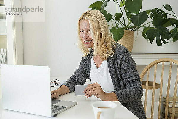 Lächelnde Frau mit Kreditkarte und Laptop zu Hause