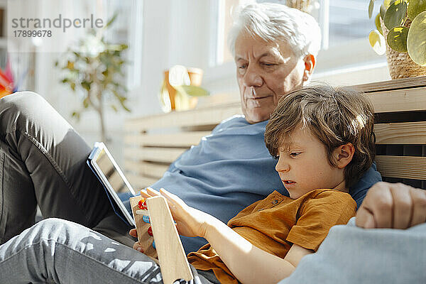 Großvater schaut Enkel mit Abakus an  der auf Sofa sitzt