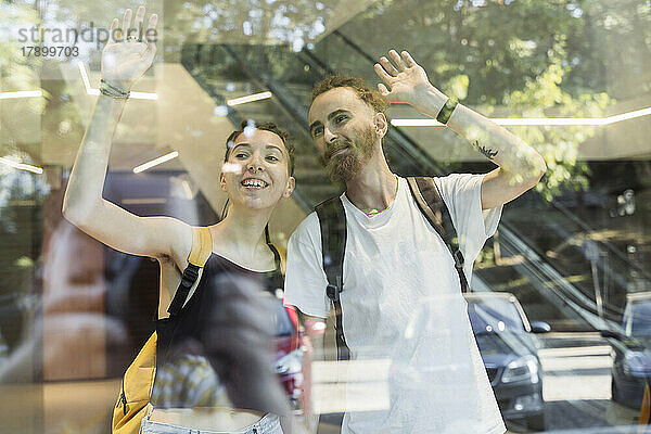 Couple hipster waving through glass window