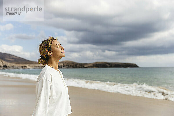 Frau steht mit geschlossenen Augen am Strand