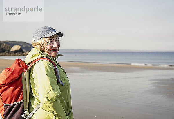Glückliche ältere Frau mit Rucksack steht am Strand