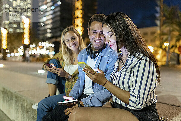 Lächelnde junge Männer und Frauen schauen Freunde mit Smartphone an