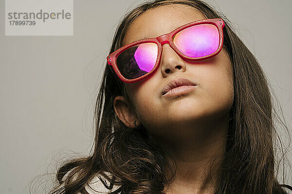 Selbstbewusstes Mädchen mit Sonnenbrille vor grauem Hintergrund