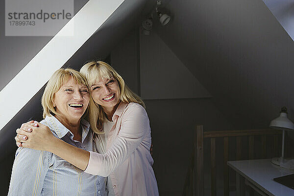 Fröhliche blonde Frau umarmt Mutter  die zu Hause steht