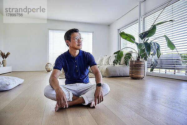 Smiling mature man sitting cross-legged on floor at home