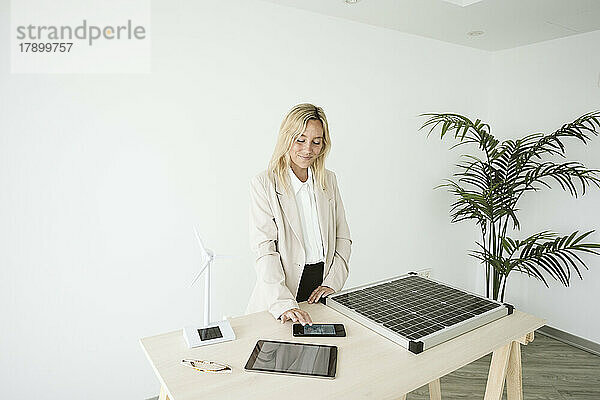 Frau im Büro mit Solarpanel und Windturbinenmodell auf dem Schreibtisch